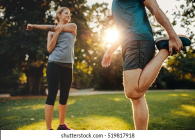 Shot of young man and woman stretching in the park. Young couple warming up in morning.