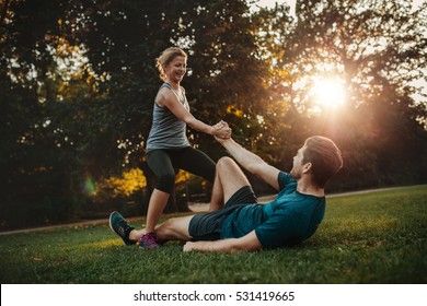 Shot Of Young Woman Helping Man To Get Up From Ground. Healthy Young Couple At Park Exercising Together.