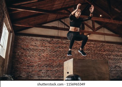 Shot of a young woman jumping onto a box as part of exercise routine. Fitness woman doing box jump workout at gym.