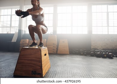 Shot of a young woman jumping onto a box as part of exercise routine. Fitness woman doing box jump workout at crossfit gym. - Powered by Shutterstock