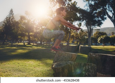 Shot of a young woman jumping onto wooden log at the park. Sportswoman doing exercise in nature on a sunny day. Box jumps. - Powered by Shutterstock