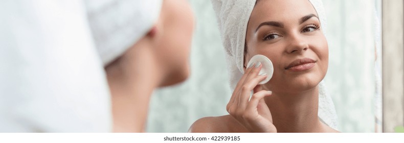 Shot of a young woman removing her makeup and looking at herself in a mirror
