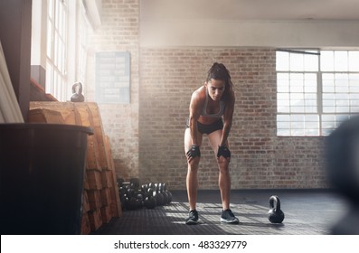 Shot of young woman in sportswear bending with her hands on knees at the gym. Fitness woman looking tired after intense crossfit workout. - Powered by Shutterstock