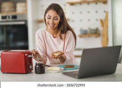 Foto de una joven que esparce mantequilla en tostada en su cocina.