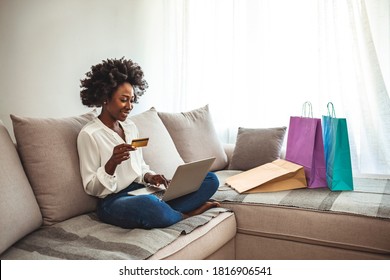 Shot Of A Young Woman Using Her Credit Card To Make An Online Payment At Home. Wireless Retail Therapy. Young Woman Sitting On Her Sofa At Home And Using Her Tablet For Online Shopping