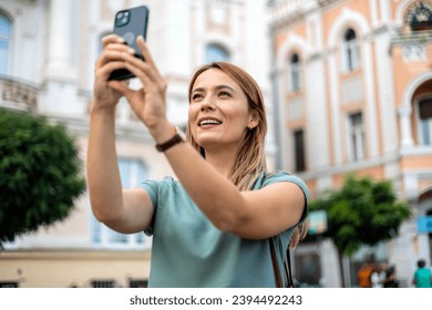 Shot of a young woman using a smartphone and taking a selfie while out in the city. - Shutterstock ID 2394492243