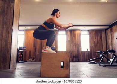 Shot of young woman working out with a box at the gym. Female athlete box jumping at a crossfit gym.