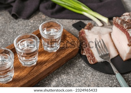 Shots with cold vodka and bacon on grey background