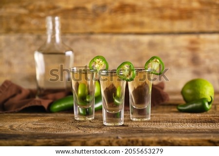 Shots of tasty tequila with jalapeno peppers on wooden background
