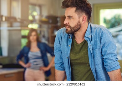 Should I Stay Or Walk Away. Shot Of A Young Man Looking Upset After A Fight With His Wife Who Is Standing In The Background.