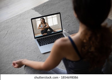 Shoulder back top view young woman sitting on floor carpet in lotus position, practicing yoga exercises online with professional female instructor, internet educational fitness courses concept. - Powered by Shutterstock