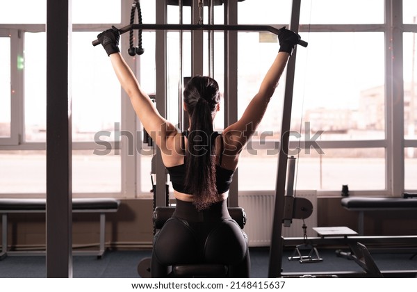 Shoulder lowering machine. Fitness woman is training\
in the gym. Upper body strength exercise for the upper back. back\
view without face