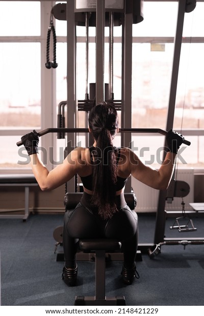 Shoulder\
lowering machine. Fitness woman is training in the gym. Upper body\
strength exercise for the upper back. back\
view