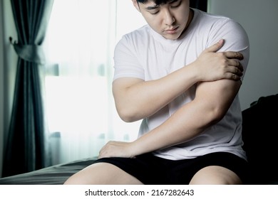 Shoulder pain, arm pain, man with musculoskeletal problems, concept of health care and medicine Asian man sitting in bed and holding a painful arm muscle with one hand. from sleeping the wrong way  - Shutterstock ID 2167282643
