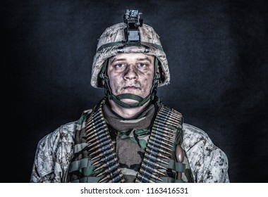 Shoulder Portrait Of Experienced Army Soldier, Military Conflict Veteran, Skilled Marine Fighter In Ragged Camouflage Uniform, Advanced Helmet And Ammo Belts On Chest, Studio Shot On Black Background