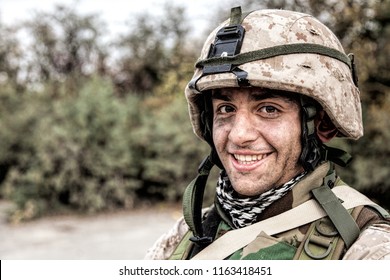 Shoulder Portrait Of Happy Smiling Young Soldier In Battle Helmet With Scratches On Camouflage, Equipped U.S. Army Contractor, Marine Corps Infantryman With Dirty Face Looking At Camera With Friendly