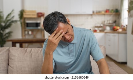shoulder portrait of unwell Asian retired male suffering chronic headache at home. he props his head and buries face in hand with discomfort on the sofa. - Shutterstock ID 2156680849