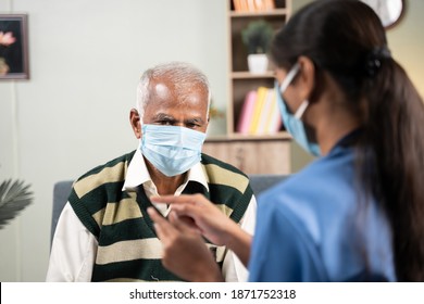 Shoulder shot of Doctor explaining how to use health app on mobile to elder man during home visit while both worn face mask - concept of senior people helath check up