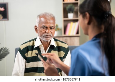 Shoulder Shot Of Doctor Explaining To Patient About Health Details By Using Mobile App On Phone During Routine Home Visit.