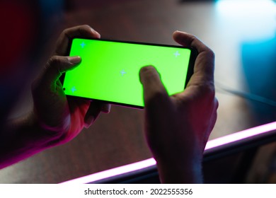 Shoulder Shot First Person View Of Gamer Playing Video Game On Green Screen Mobile Phone While Talking On Headphones At Esports Gaming Tournament.