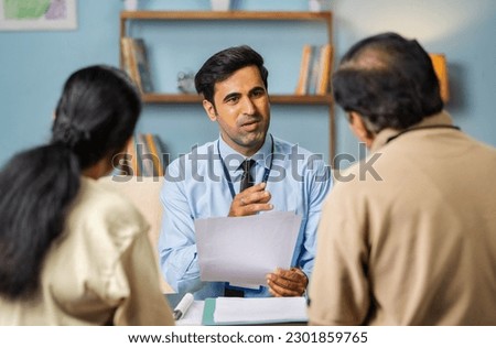 Shoulder shot, indian banker explaining about future investment plans or pension scheme offer to senio couple - concept of financial adviser, real-estate agent and consultant