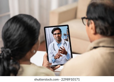 Shoulder shot of Indian Senior couple taking advice from doctor during online video call from tab at home - concept of remote health care, virtual consultation and ehealth - Powered by Shutterstock