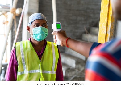 Shoulder Shot Of Man Checking Body Tempreture Of Labour With Medical Face Mask At Construction Site - Concept Of Covid19 Precaution, Back To Work And Blue Collar Jobs.