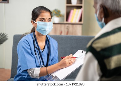 Shoulder Shot, Young Doctor Or Nurse Writing Prescription During Home Visiting To Sick Senior Man While Both Worn Face Mask Due To Coronavirus Covid-19 Pandemic As Safety Measures.