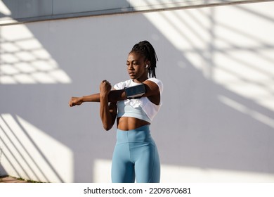 Shoulder stretching warm up exercise before running. Fit woman training outside wearing smartphone arm band and wireless earphones. - Shutterstock ID 2209870681