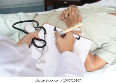 Shoulder View Of Doctor Write The Report On Clipboard With Stethoscope In Hand Examine The Symptom Of Elderly Over 80 S Asian Man Patient After Done Chemotherapy Of Liver Cancer In Hospital Ward Room