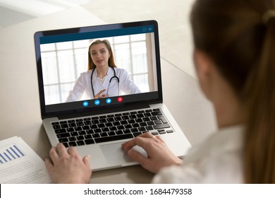 Shoulder view young woman consulting with family therapist doctor general practitioner online via video call on laptop after feeling first virus illness symptoms, medical insurance, covid19 outspread. - Shutterstock ID 1684479358