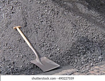 A Shovel Left Laying on a Large Pile of a Coal Stock Pile.