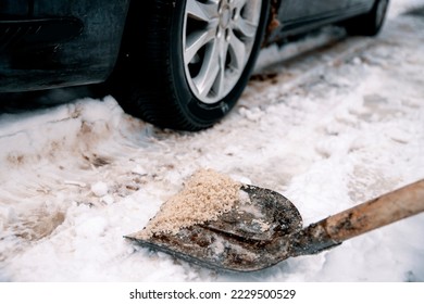 Shovel with salt on snowy driveway to protect from slippery. Winter snow cleaning the road outside. Applying Rock Salt ( Gritting ) to an Icy road for safe car traffic. De icing Copy space