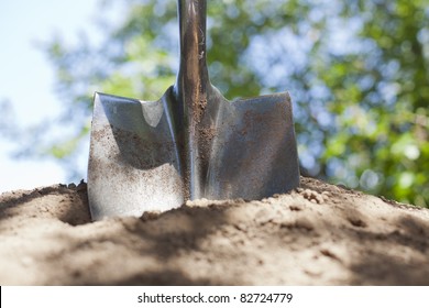 A Shovel Is Stuck In A Pile Of Dirt With Bokeh In The Background.