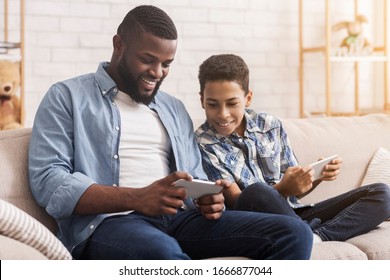 Show Me Your Score. Black Preteen Boy Competing In Video Games On Smartphones With His Dad, Sitting On Couch At Home, Enjoying Weekend