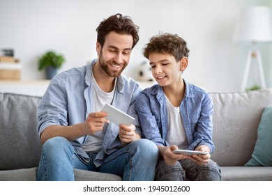 Show Me Your Score. Boy Competing With Dad In Online Video Games On Smartphones, Sitting On Couch At Home. Guy Looking At Father's Phone, Enjoying Spending Time Together On Weekend