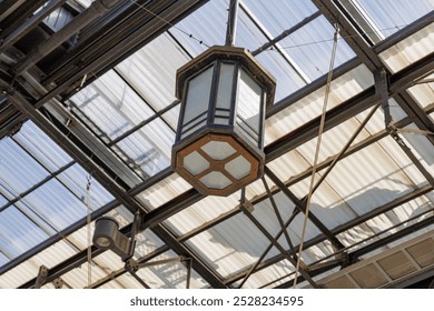 A Showa era, vintage light fixture hangs in the rafters of an outdoor arcade in downtown Nagoya. Hexagonal shaped, the rust colored light features a metal and opaque glass structure. - Powered by Shutterstock