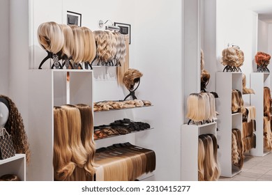 Showcase of natural looking wigs in different colors fixed on the metal wig holders in beauty salon. Row of mannequin heads with variation shades hair on shelf in wig shop