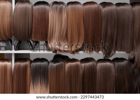 Showcase of natural looking wigs in different shades of brunette fixed on the wig holders in beauty salon. Row of mannequin heads with variation colors hair on shelf in wig shop