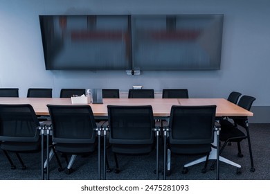 The showcases a modern, professional conference room setting.Room features a large wooden table surrounded by black mesh office chairs, indicating a space designed for meetings or collaborative work. 