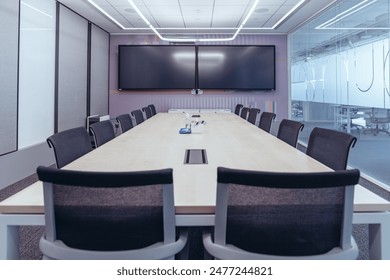 The showcases a modern, professional conference room setting.Room features a large wooden table surrounded by black mesh office chairs, indicating a space designed for meetings or collaborative work. 
