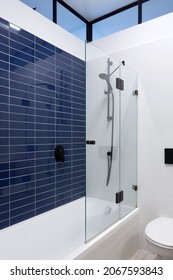 Shower With Blue Wall Tiles, Faucet And Black Shower Head, Toilet, White Bath And Elongated Window On Black Frame