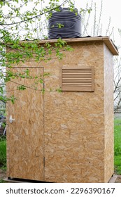a shower cabin made of OSB boards, with a large barrel for heating water from the sun, in the courtyard of the house in spring. Building a summer shower. - Shutterstock ID 2296390167