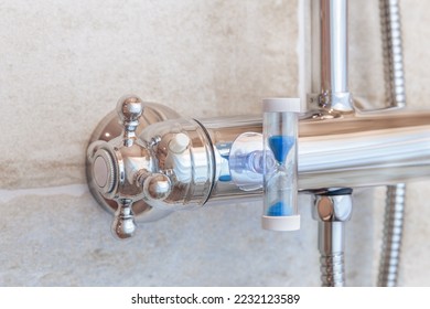 A shower faucet in the bathroom with an hourglass attached to cut back shower time in order to save water and energy.
