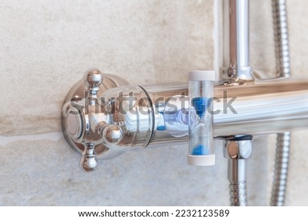 A shower faucet in the bathroom with an hourglass attached to cut back shower time in order to save water and energy.