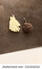 Shower sponge gloves and wisp of bast handing on the hook on a marble brown wall in a bathroom