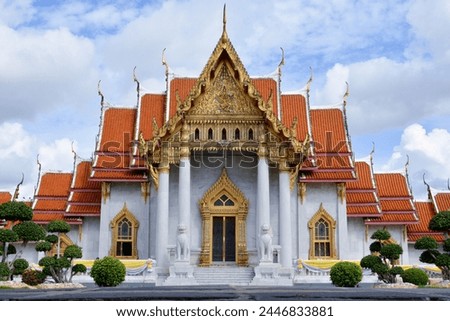 showing beautiful white and gold temple with a red roof. With a lion statue with a red mouth in front.
The temple is a Buddhist temple, Wat Benchamabophit, a marble temple in Bangkok, 