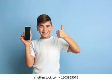 Showing blank phone's screen. Caucasian boy portrait isolated on blue studio background. Beautiful teen male model in white shirt posing. Concept of human emotions, facial expression, sales, ad. - Shutterstock ID 1603965076