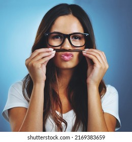 Showing Her Quirky Side. Studio Portrait Of An Attractive Young Woman Playfully Making A Moustache With Her Hair Against A Blue Background.