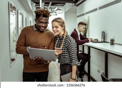 Showing Information. Smiling African American Guy In Clear Glasses Holding Laptop While Interested Colleague Staring On It